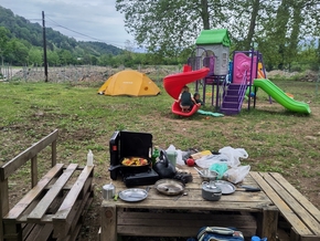 Notre tente à côté de jeux pour enfants, toboggan, cabane. En premier plan, une table en palettes avec nos affaires de cuisine