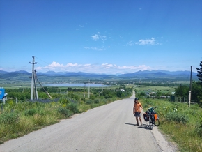 Léon nous attend à côté de son vélo, vue de haut sur le lac et le Caucase au loin.